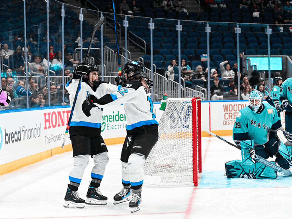 Two Toronto players celebrate a goal against New York with a group hug. They are wearing white away uniforms.