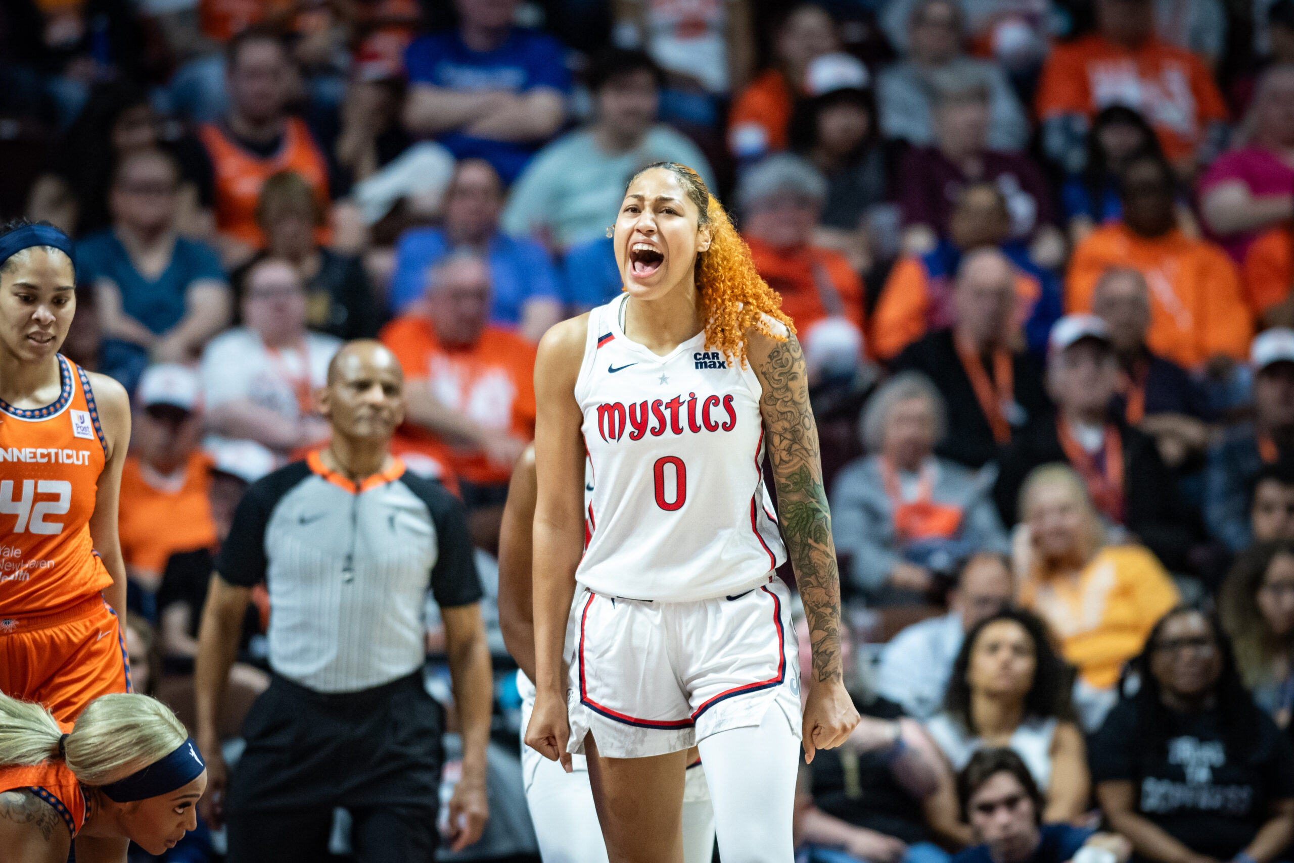 Shakira Austin yells in celebration in front of a packed Connecticut Sun crowd during a WNBA game, while Sun players at the edge of the frame catch their breath