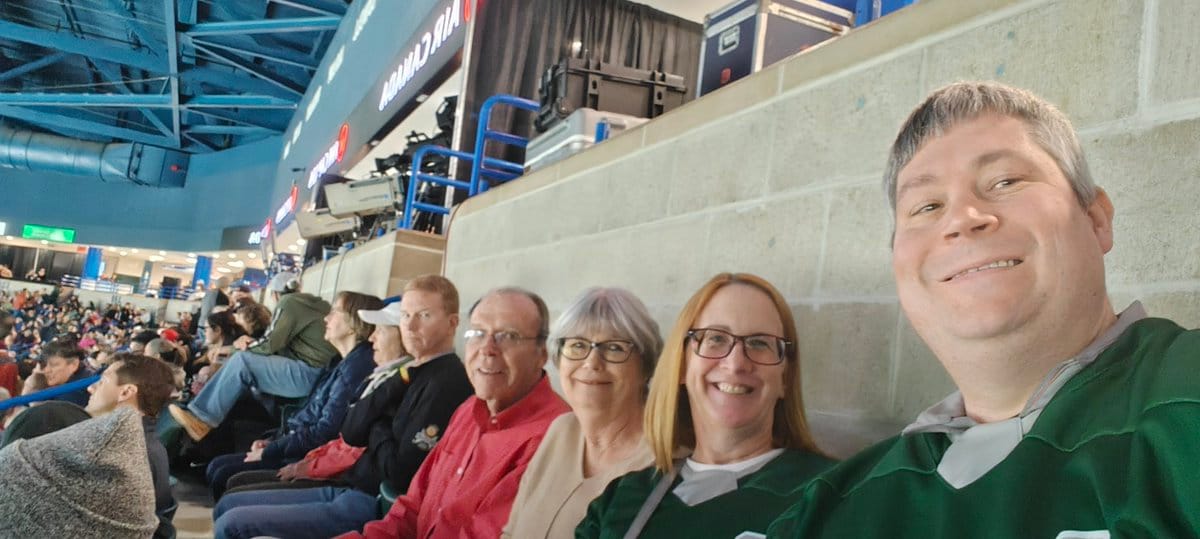 A selfie of Wayne and Kerry in green PWHL Boston jerseys sitting next to another man and woman who are their friends. They're all smiling and looking at the camera.