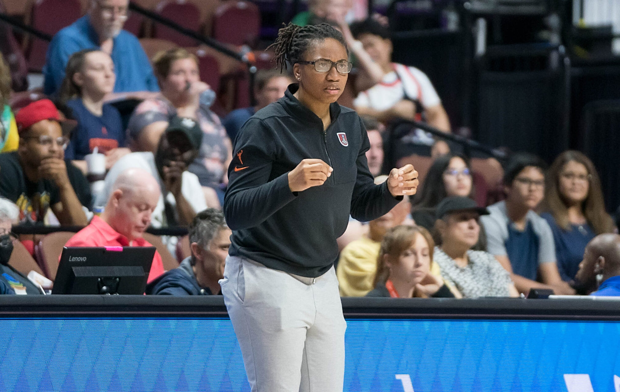 Atlanta Dream head coach Tanisha Wright stands on the sideline and watches the game with her hands loosely clenched at chest level.