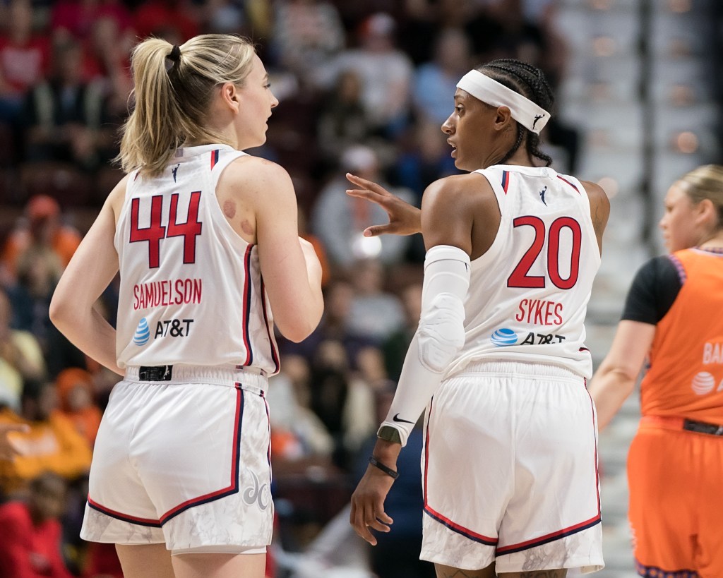 Washington Mystics guard Brittney Sykes and wing Karlie Samuelson are photographed from behind looking at one another. Sykes has a hand out in front of her as she talks.