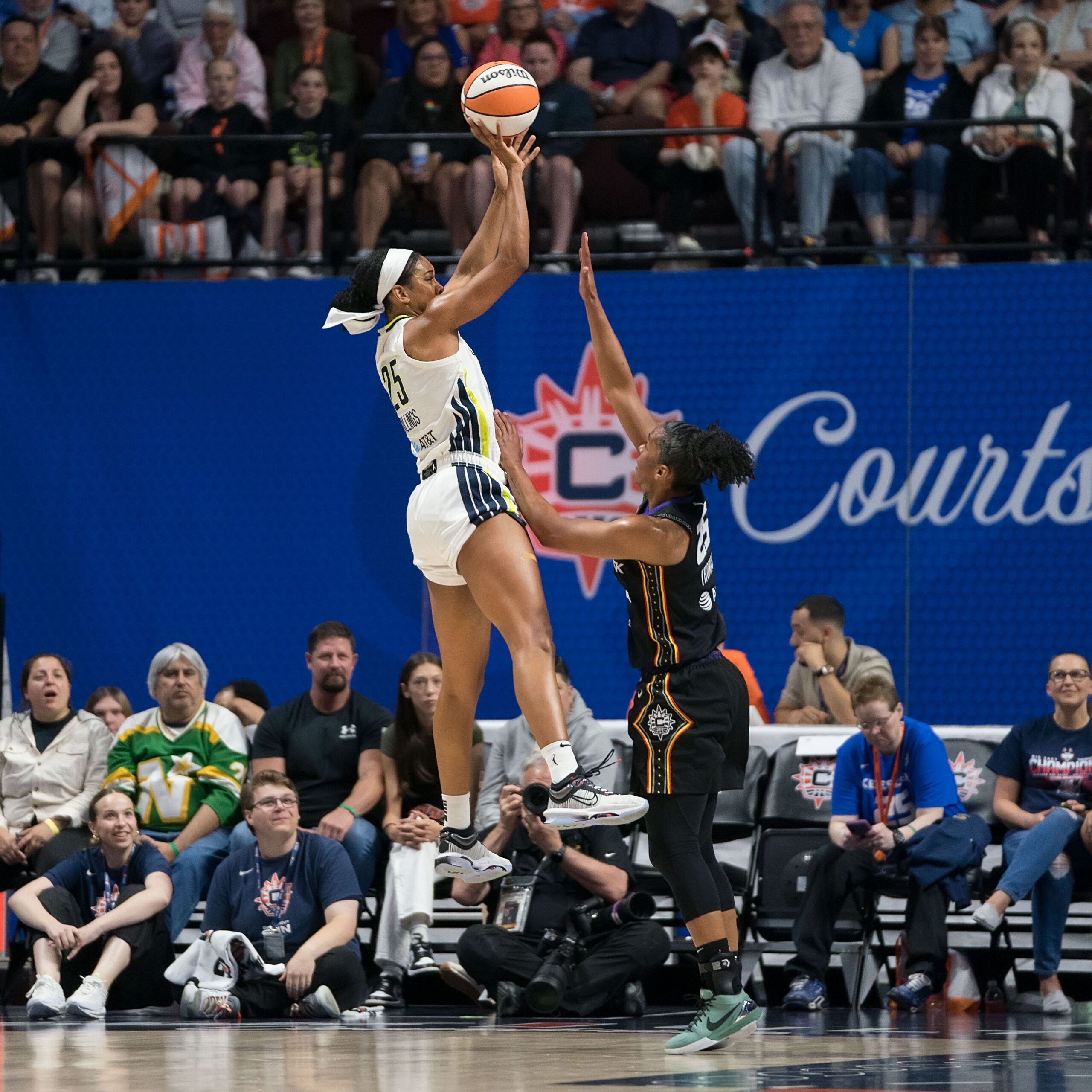 During a game at Mohegan Sun Arena, Wings forward Monique Billings (25) jumps to shoot the ball over Sun forward Alyssa Thomas (25) who is defending.