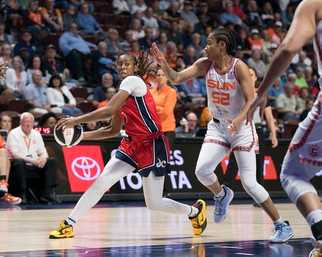 Washington Mystics guard Ariel Atkins stands on two feet, holding the ball on the right side of her body, as she looks cross-court for a possible pass.
