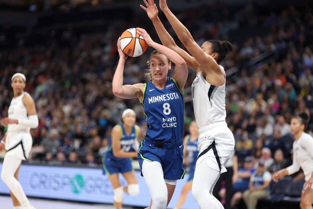 Minnesota Lynx forward Alanna Smith holds the ball over her head with two hands and looks for an outlet as Las Vegas Aces center Kiah Stokes pressures her.