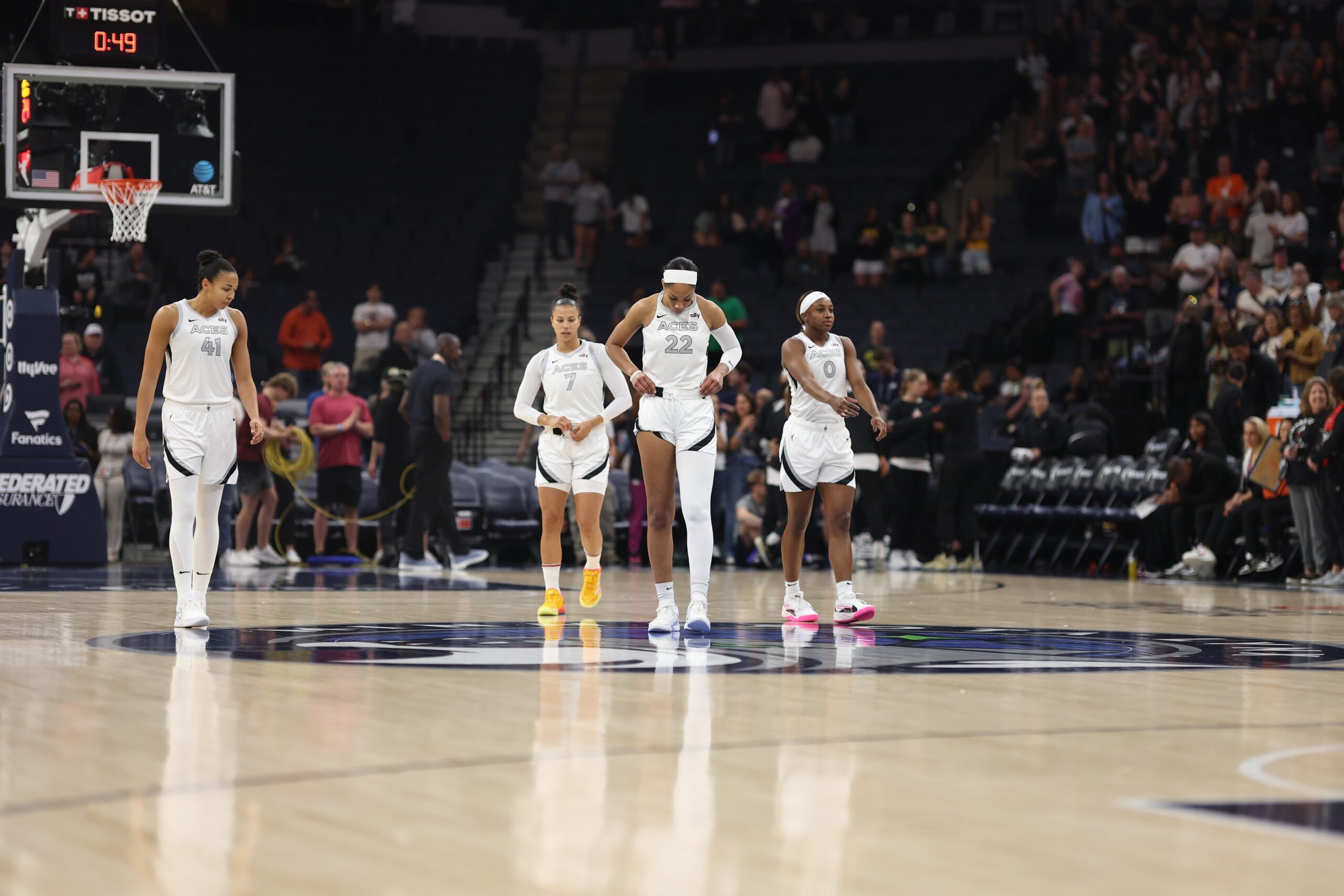 Four Las Vegas Aces players walk onto the court, looking down at the ground or straight ahead.
