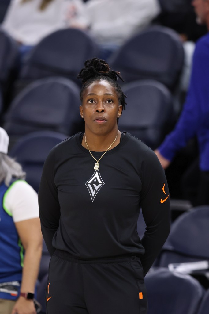 Las Vegas Aces guard Chelsea Gray stands on the sideline in sweats with her arms behind her back.