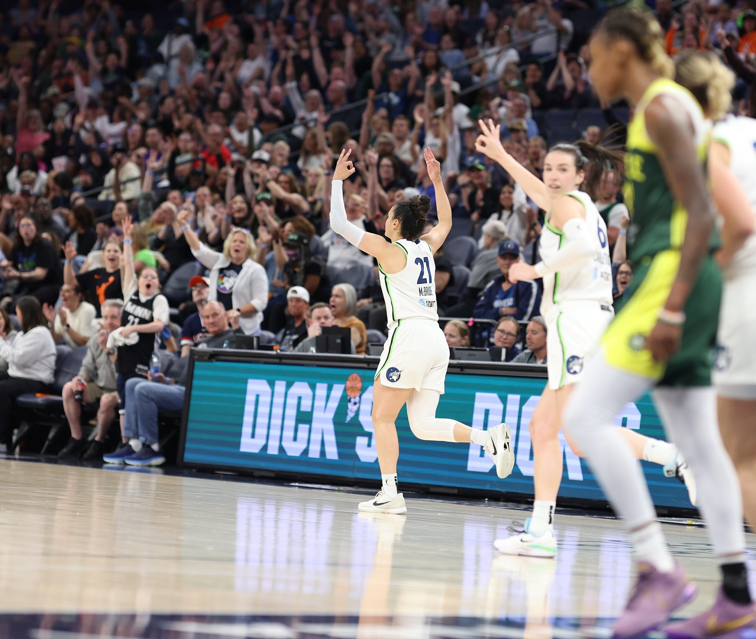 Minnesota Lynx guard Kayla McBride is shown with her back to the camera, running down the court with both hands up in celebration.