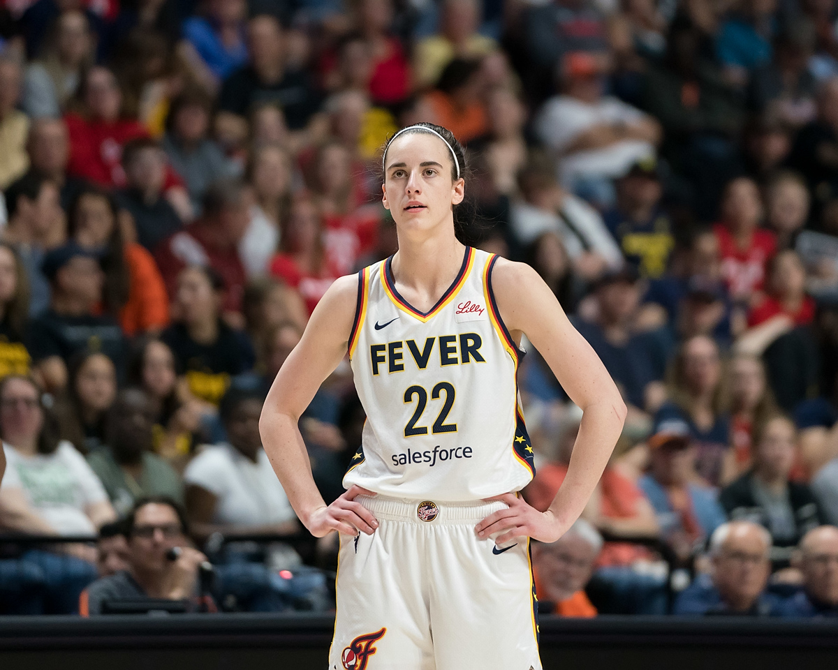 Indiana Fever guard Caitlin Clark stands with her hands on her hips and looks straight ahead.