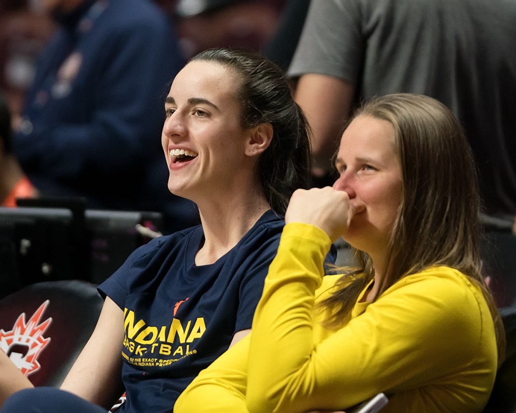 Indiana Fever guard Caitlin Clark sits on the bench and laughs with assistant coach Jessie Miller.
