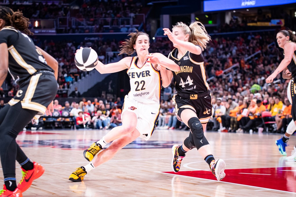 Indiana Fever guard Caitlin Clark dribbles the ball with her right hand and sticks out her tongue as she exerts herself trying to drive by Washington Mystics wing Karlie Samuelson.