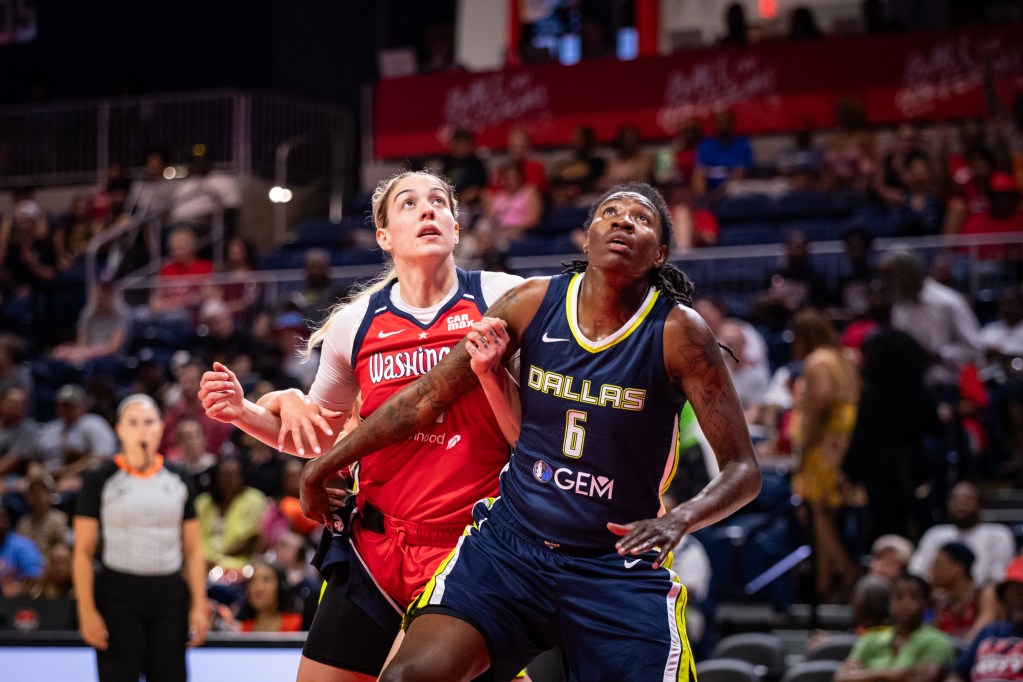 Dallas Wings forward Natasha Howard is a half-step in front of Washington Mystics forward Emily Engstler and reaches her right arm out to box out Engstler. Both players look up, watching the flight of the ball.