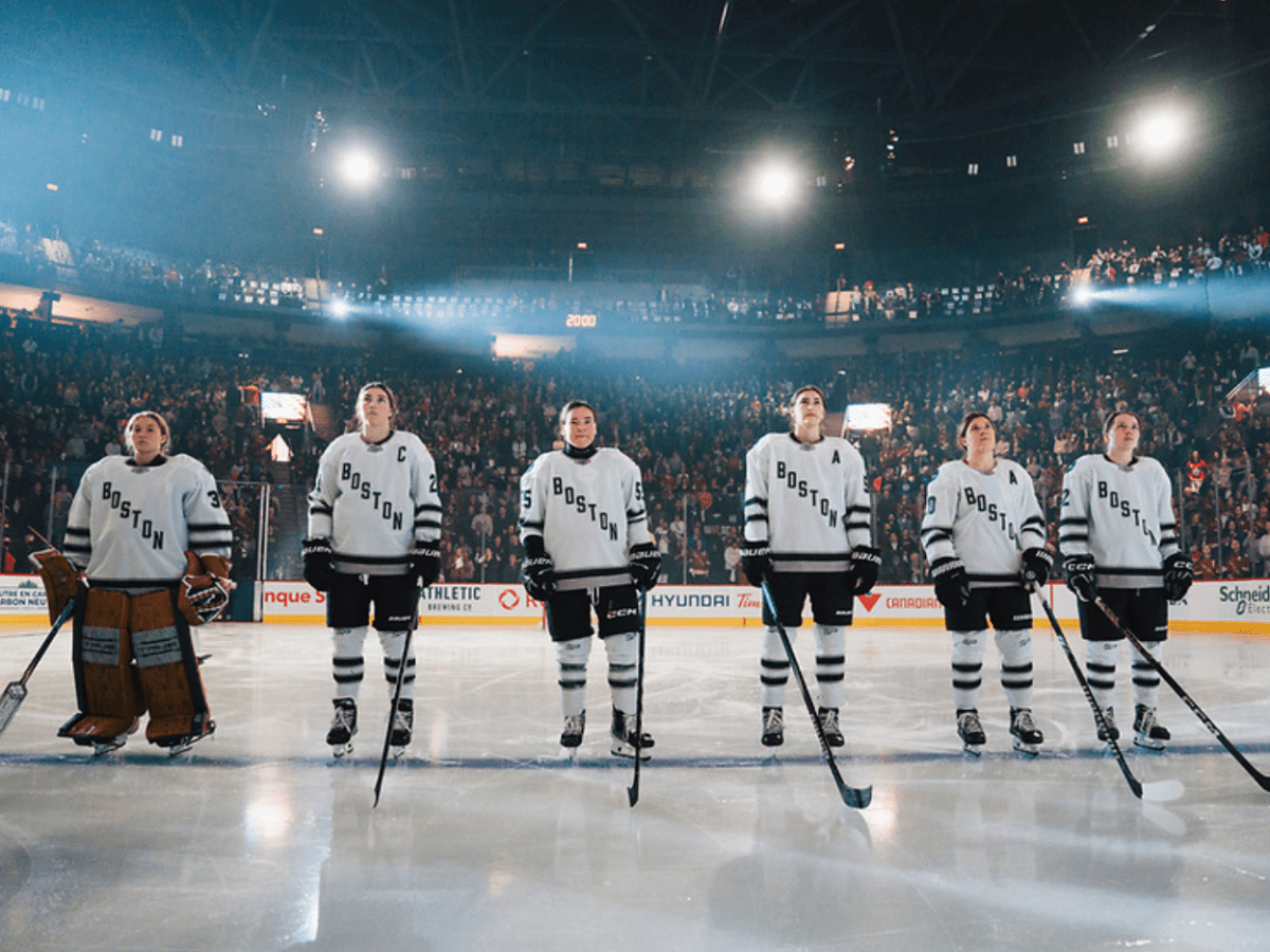 Five Boston players stand on the blue line with their helmets off. They're wearing white away uniforms.