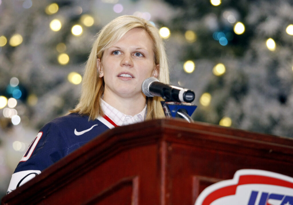 USA ice hockey legend Natalie Darwitz stands at a podium in USA hockey gear