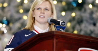 USA ice hockey legend Natalie Darwitz stands at a podium in USA hockey gear