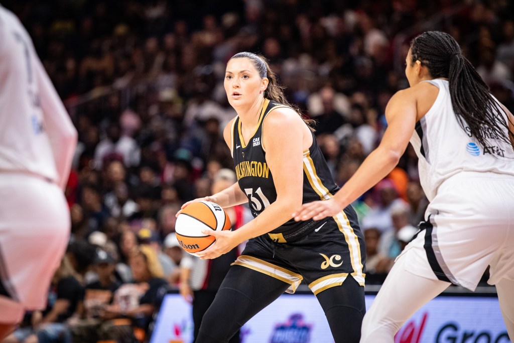 Washington Mystics center Stefanie Dolson holds the ball with both hands near her right hip. Her eyes are up as she looks for her next move. Las Vegas Aces center Kiah Stokes is in the frame but not pressuring her super tightly.