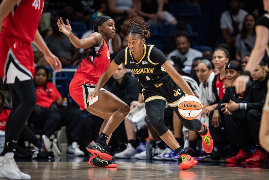 Washington Mystics guard Ariel Atkins dribbles the ball with her left hand. Las Vegas Aces guard Jackie Young slides her feet laterally, but Atkins appears to be a step ahead of her.