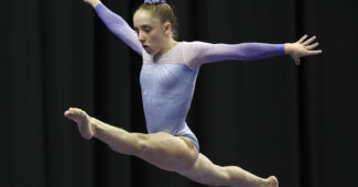 Syd Morris wears a purple leotard and performs a split leap on the balance beam at the 2019 U.S. National Championships.
