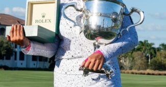 Lilia Vu smiles for a photo. She holds a large silver trophy in one hand and an open Rolex box in the other.