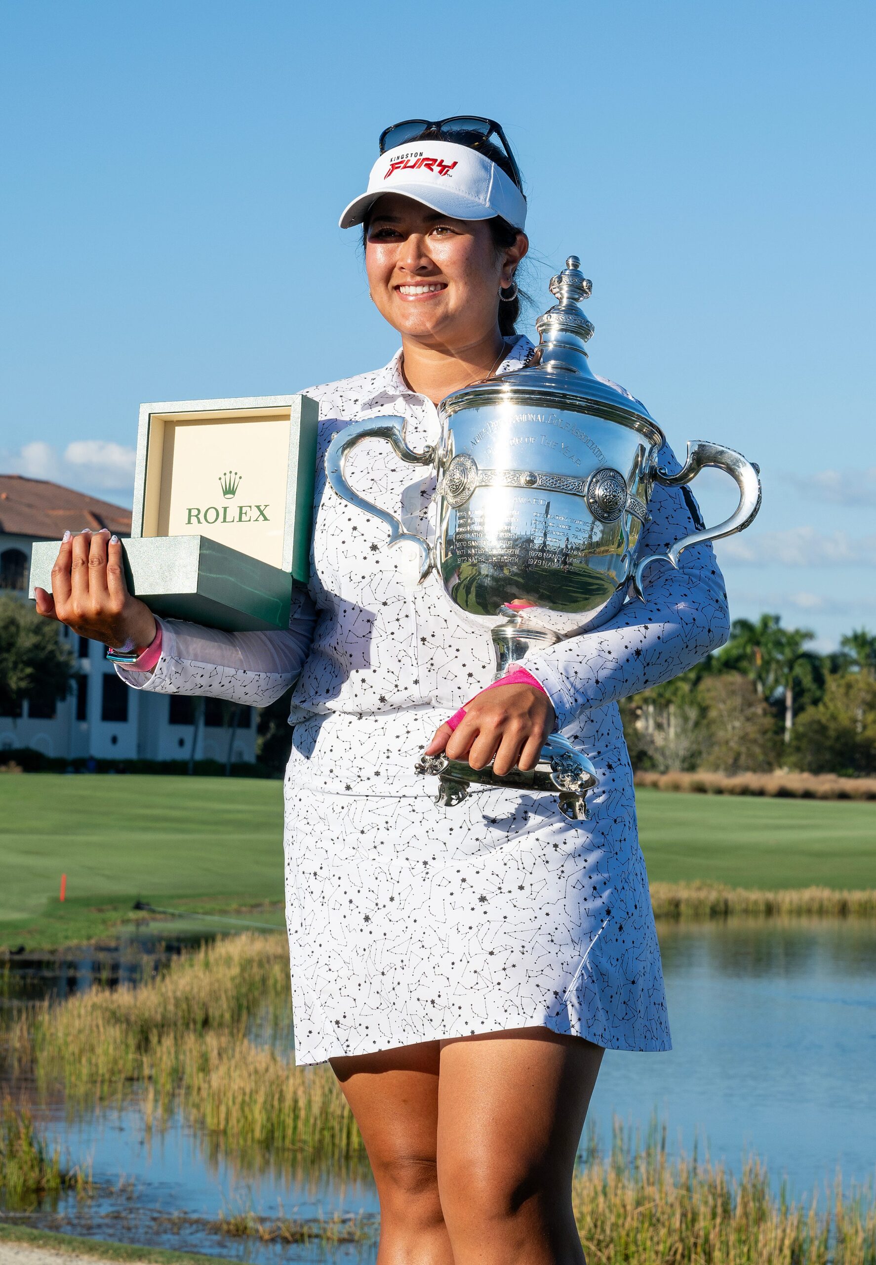 Lilia Vu smiles for a photo. She holds a large silver trophy in one hand and an open Rolex box in the other.