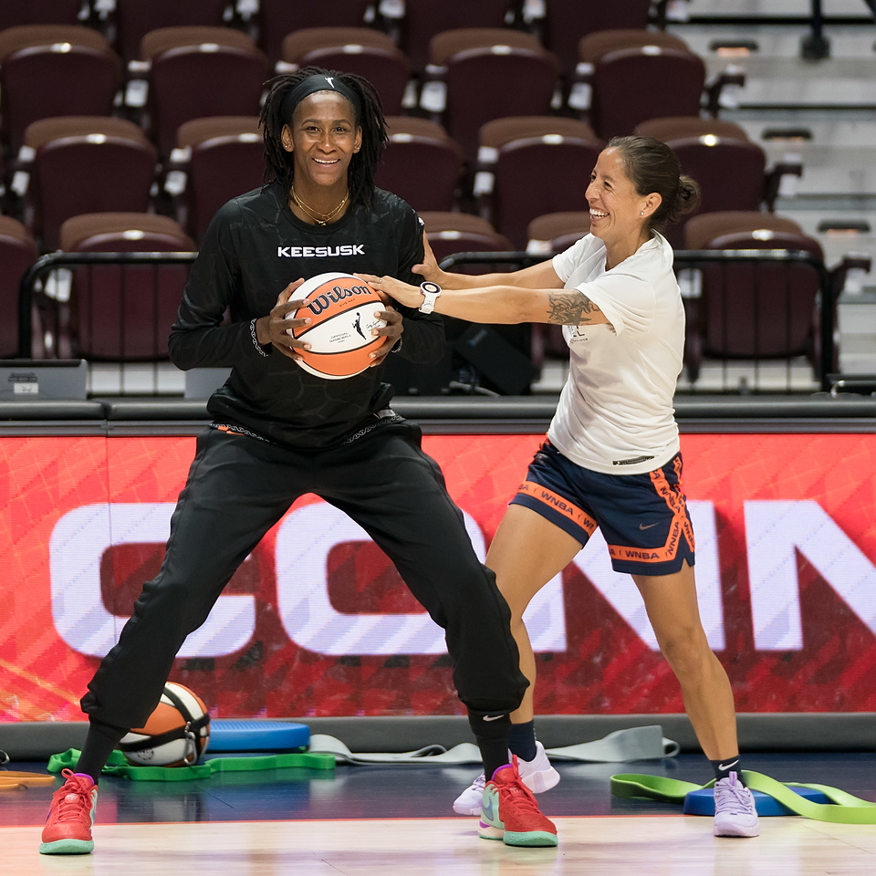 Before a game, Connecticut Sun strength and conditioning coach Analisse Rios taps an orange and white basketball held by Sun center/forward Astou Ndour-Fall.