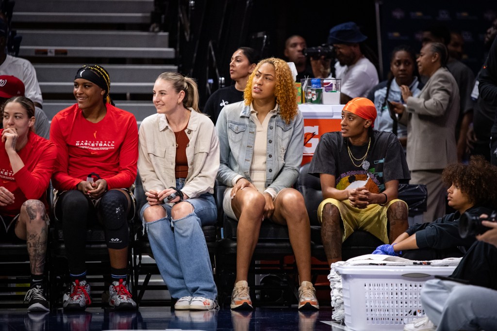 Washington Mystics players watch the action from the bench. Some are smiling, but others look more concerned.