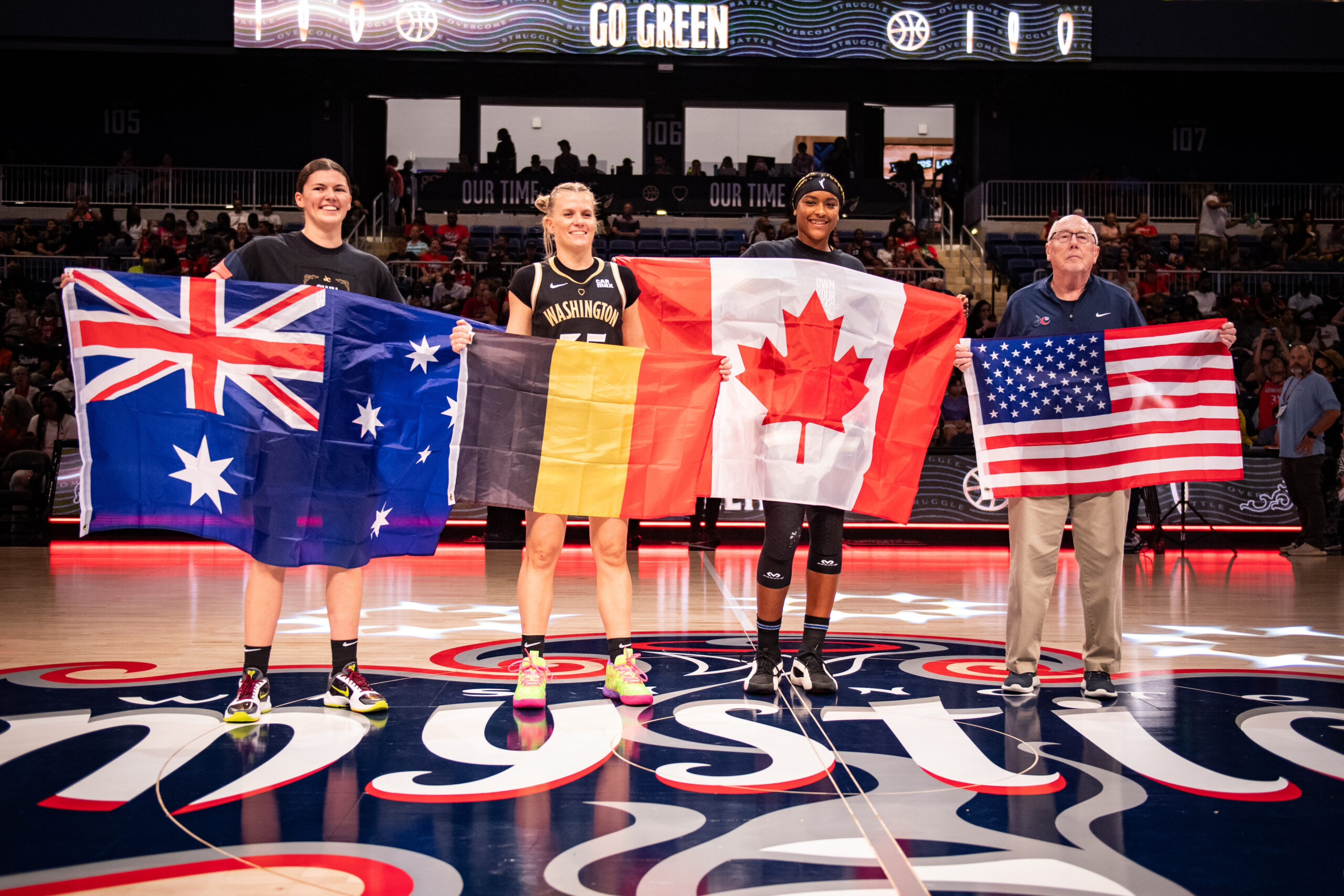 Washington Mystics players Jade Melbourne, Julie Vanloo and Aaliyah Edwards and general manager Mike Thibault posed for a photo at center court before heading to the 2024 Paris Olympics. Each held the flag of the country they represent: Australia, Belgium, Canada and the United States, respectively.