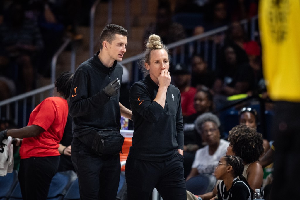 Las Vegas Aces Lead Athletic Trainer, Dr. Bryson Creer, and Director of Health and Performance, Dr. Ciara Burgi, both wearing all black, talking on the sidelines during a game.