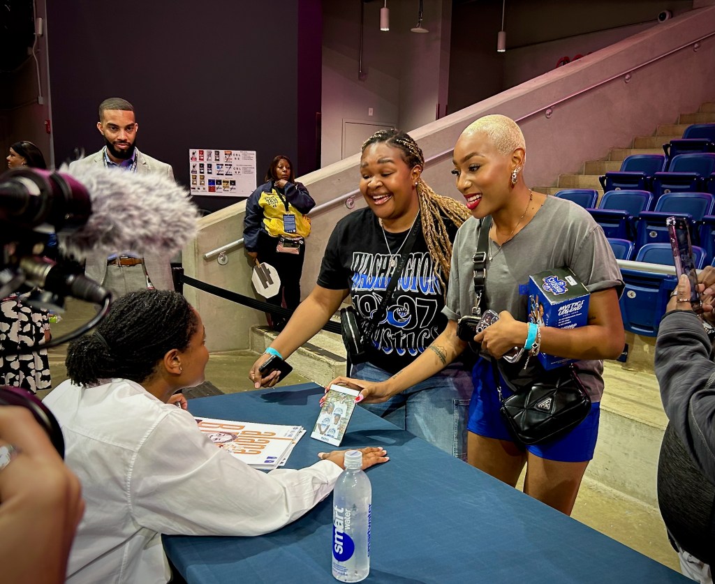 Former Washington Mystics guard/forward Alana Beard sits at a table during a postgame autograph signing. Two fans show her a photo of the three of them from 2008.
