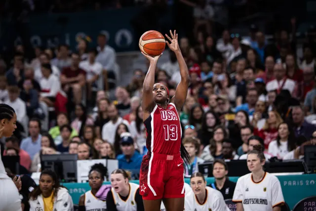 Jackie Young rises to shoot a jump shot in a red No. 13 Team USA jersey in front of the Team Germany bench looking on behind her.