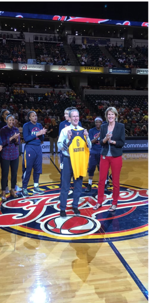 Indiana Fever director of medical services and head athletic trainer Todd Champlin holds up a personalized yellow Fever jersey at center court.