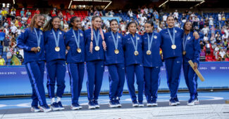 Team USA celebrates winning gold medal while standing upon the medal podium in warm-up uniforms