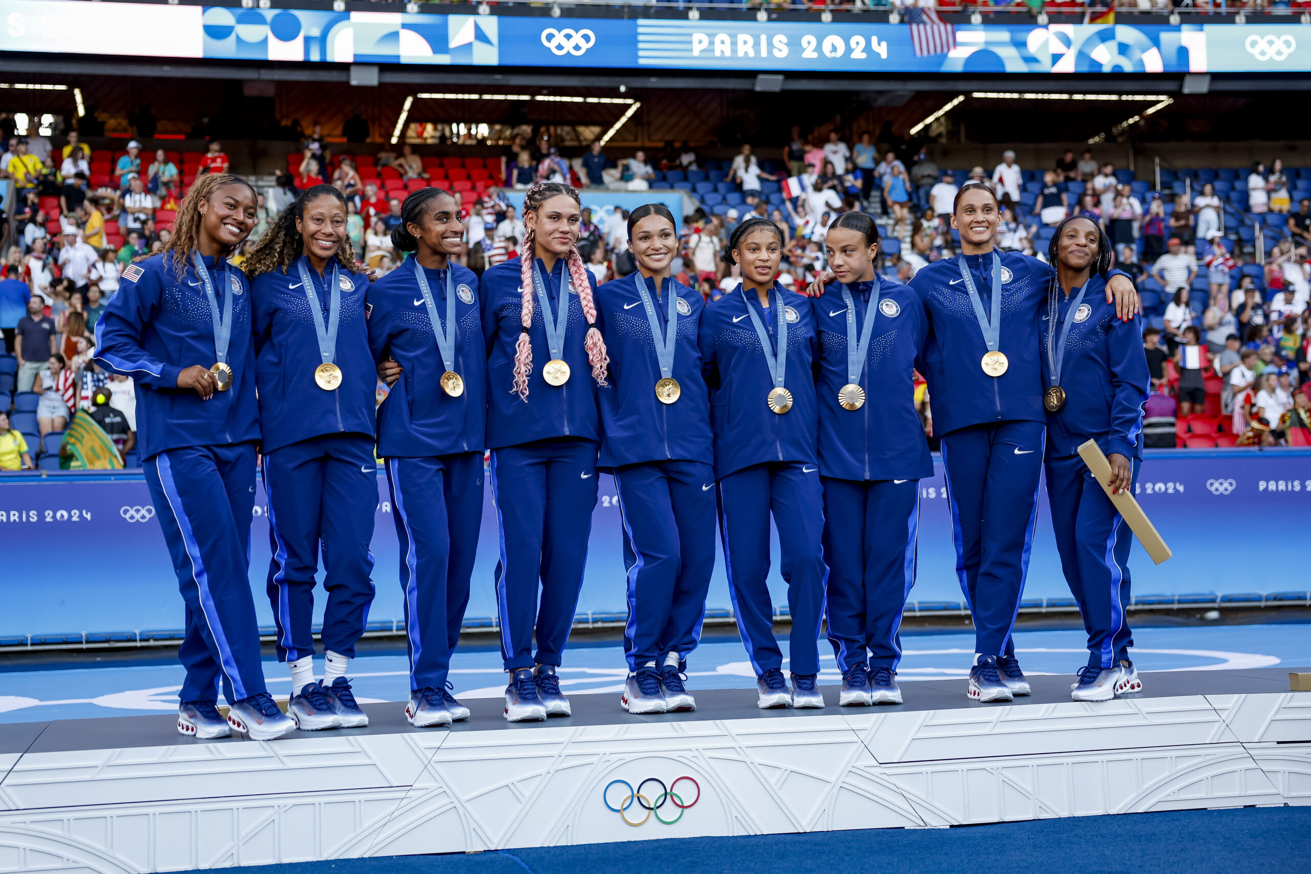Team USA celebrates winning gold medal while standing upon the medal podium in warm-up uniforms