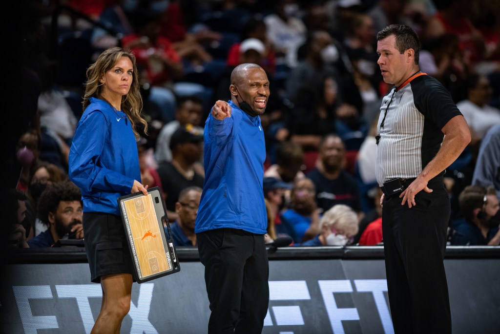 Chicago Sky vice president of operations and head strength and conditioning coach Ann Crosby holds a clipboard, stands with former Sky head coach James Wade who is pointing to the court and speaking to a referee.