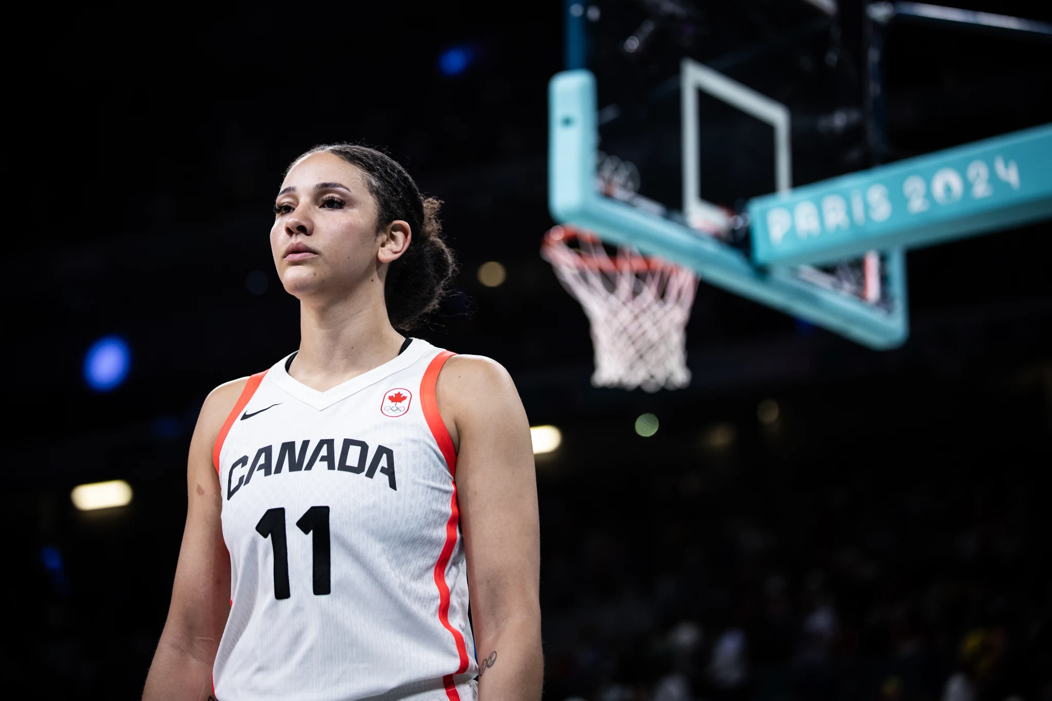 Canada's Natalie Achonwa stands alone facing away from the rim, looking stoic.