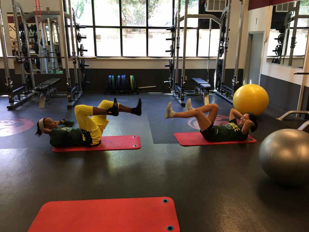Seattle Storm basketball player Jewell Loyd lays on her back with her legs in the air, training with Storm director of player performance Emily Blurton. Blurton is in the same position, mirroring Loyd.