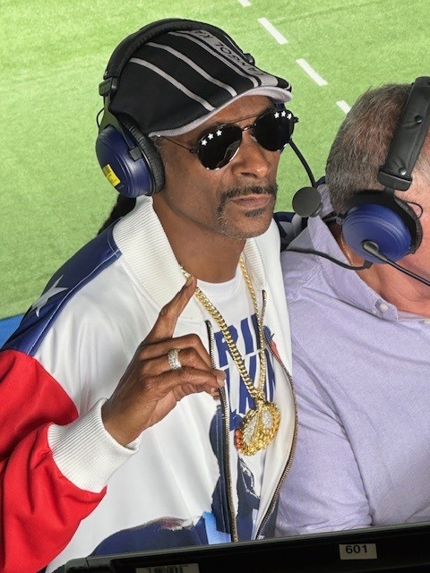 Rapper Snoop Dog is wearing a headset and motioning "No. 1"