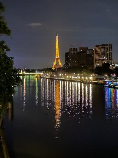 The Eiffel Tower in Paris is illuminated at night, reflecting on a body of water