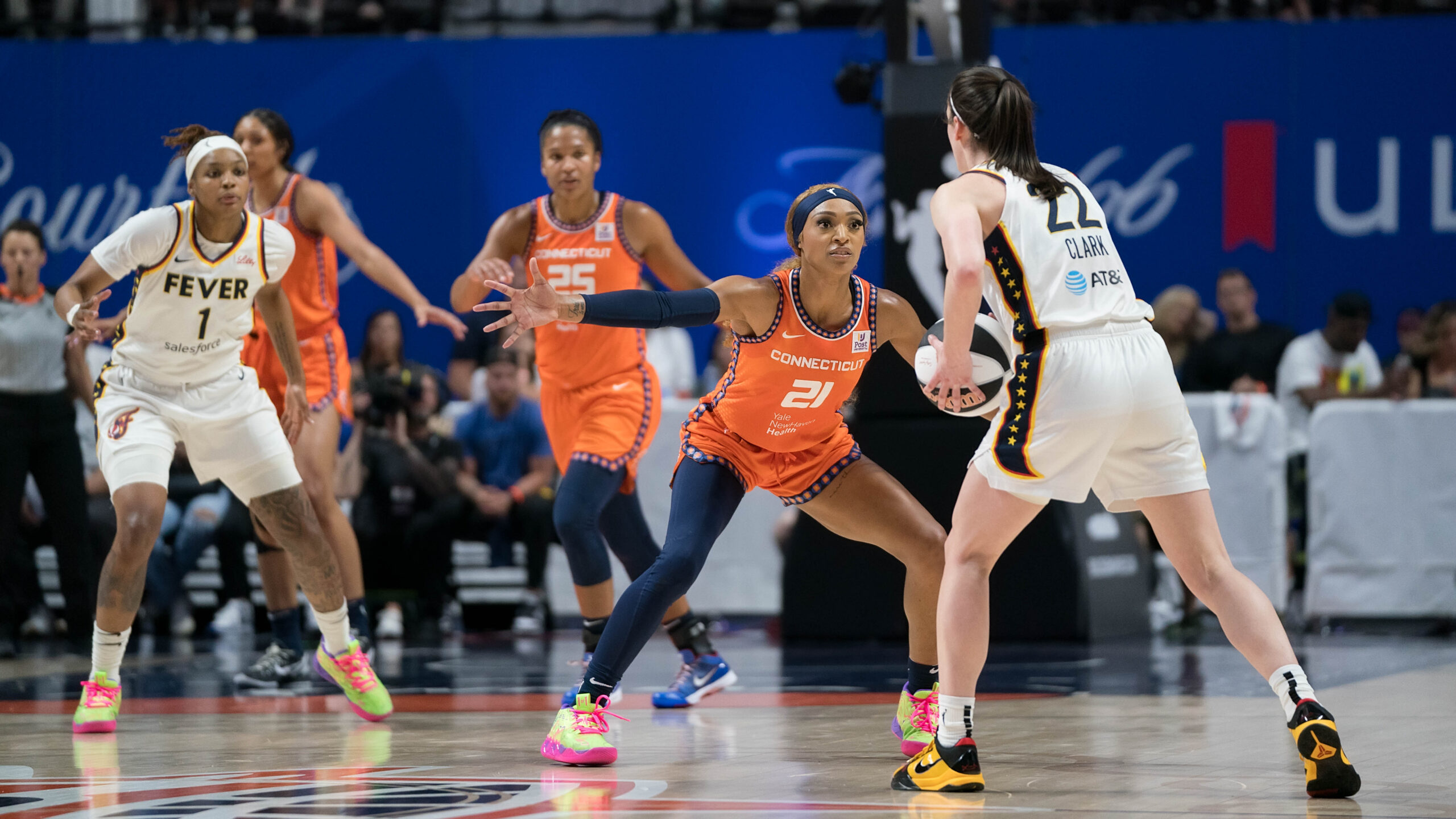 Indiana Fever guard Caitlin Clark holds the ball in front of her as Connecticut Sun guard/forward DiJonai Carrington defends her with her arms parallel to the ground and her legs in a wide stance.
