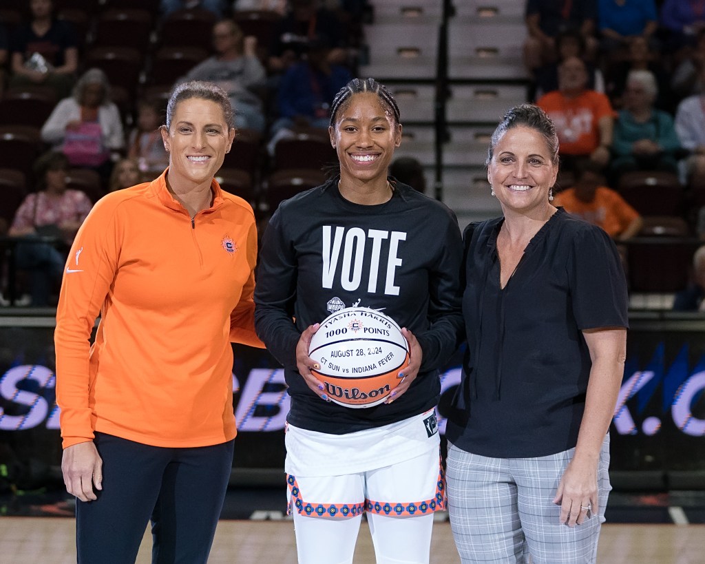 Connecticut Sun guard guard Tyasha Harris holds a ceremonial basketball honoring her 1,000th career point. She smiles and poses for a photo with head coach Stephanie White and team president Jennifer Rizzotti.