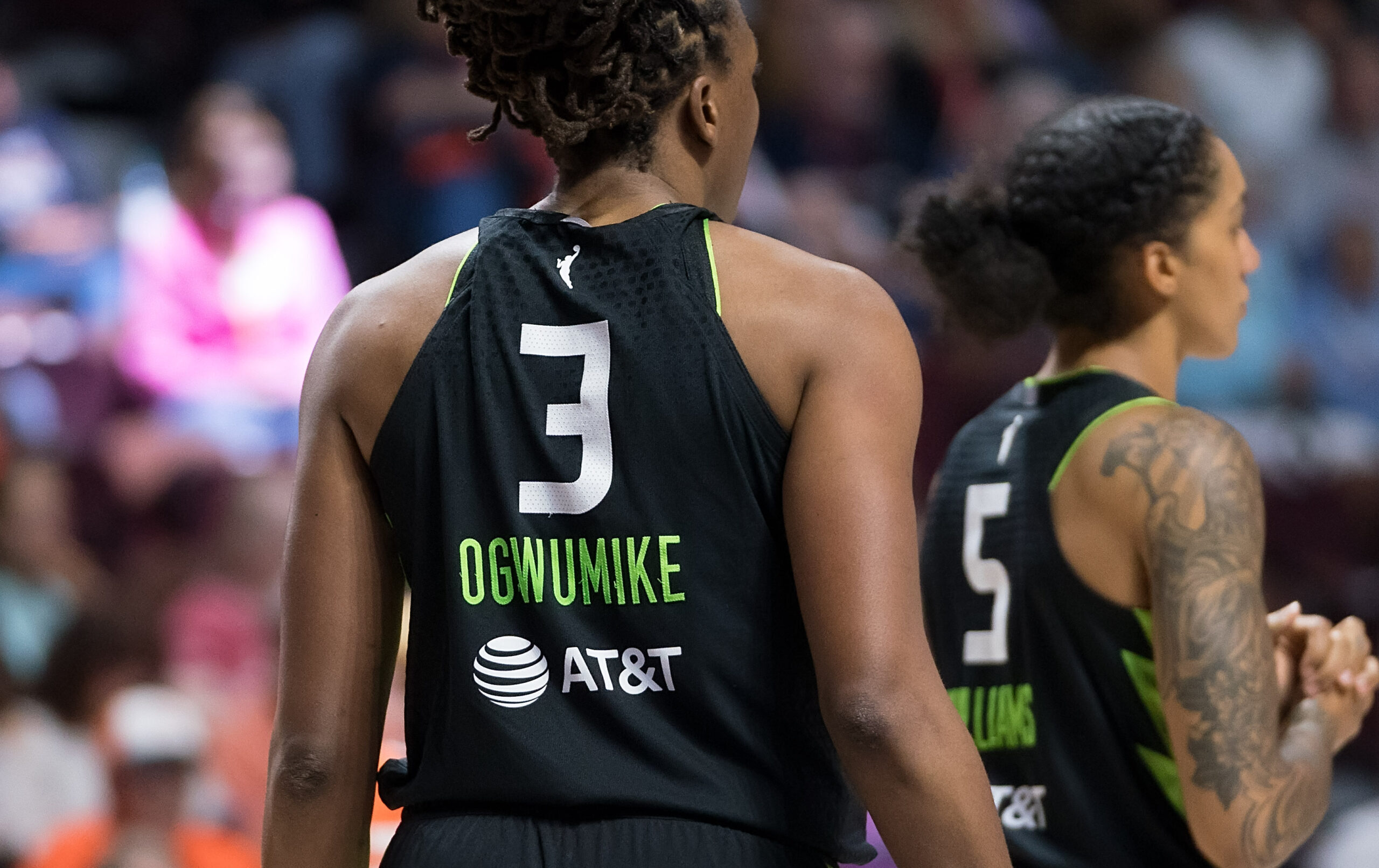 Nneka Ogwumike and Gabby Williams face away from the camera, highlighting their bright white numbers (3 and 5) on the black jerseys with their names stitched on in neon green.
