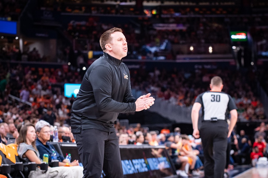 Washington Mystics head coach Eric Thibault stands on the sideline, leaning forward slightly and clapping his hands.