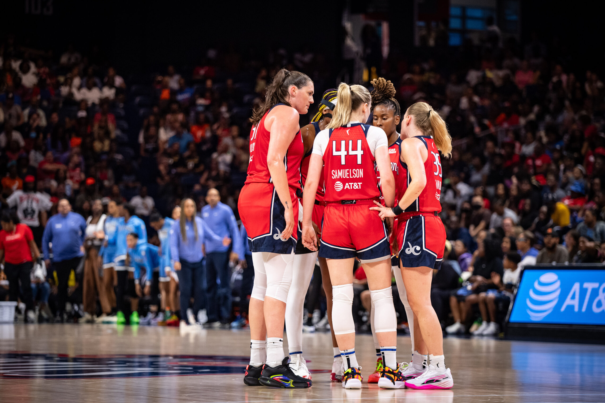 Wearing red jerseys, five Washington Mystics players huddle a little past midcourt.
