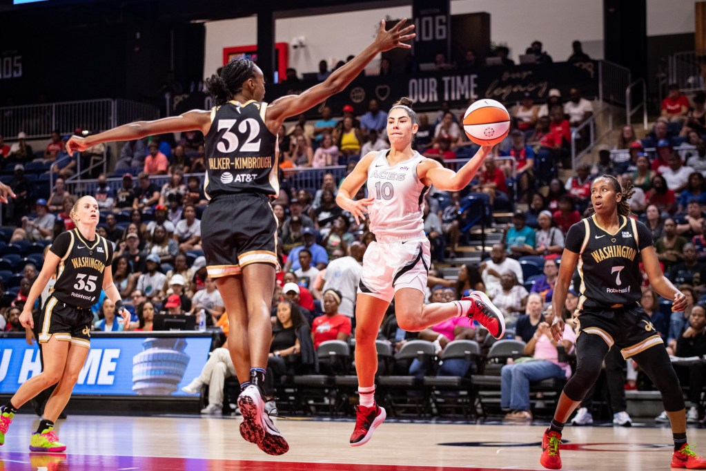 Washington Mystics guard Shatori Walker-Kimbrough jumps in the air and extends her right arm at about a 45-degree angle to try to deflect the one-handed pass that Las Vegas Aces guard Kelsey Plum is about to throw.