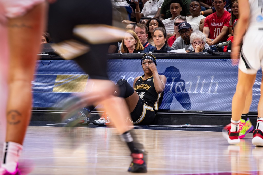 Washington Mystics forward Aaliyah Edwards sits in front of the scorer's table and adjusts her clear face mask as she waits to enter the game.