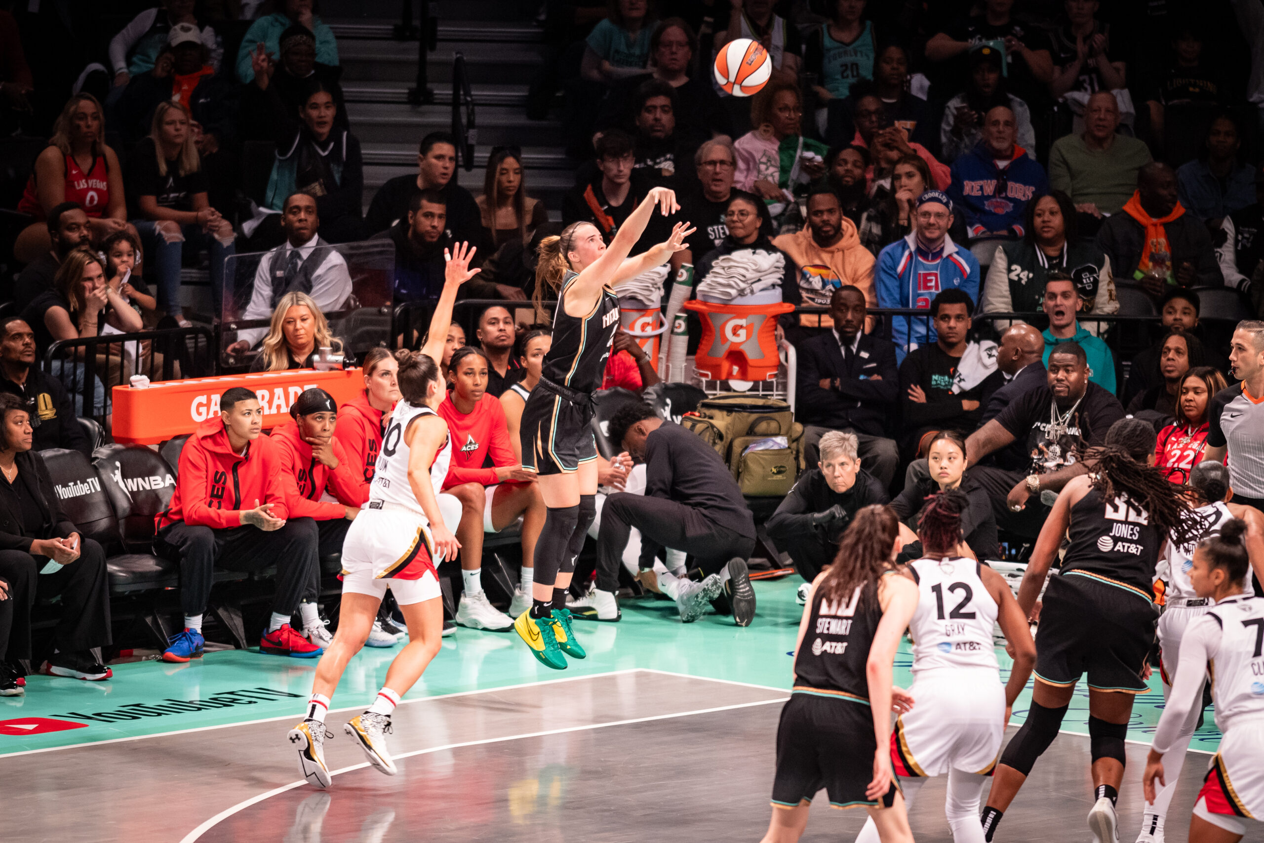 New York Liberty guard Sabrina Ionescu shoots a 3-pointer from the corner. Las Vegas Aces guard Kelsey Plum arrives too late from elsewhere on the perimeter to contest it.