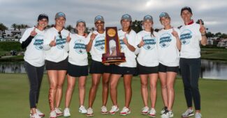 Members and coaches of the Stanford women's golf team pose, each holding up a number one with their fingers, with the NCAA National Championship held in the middle