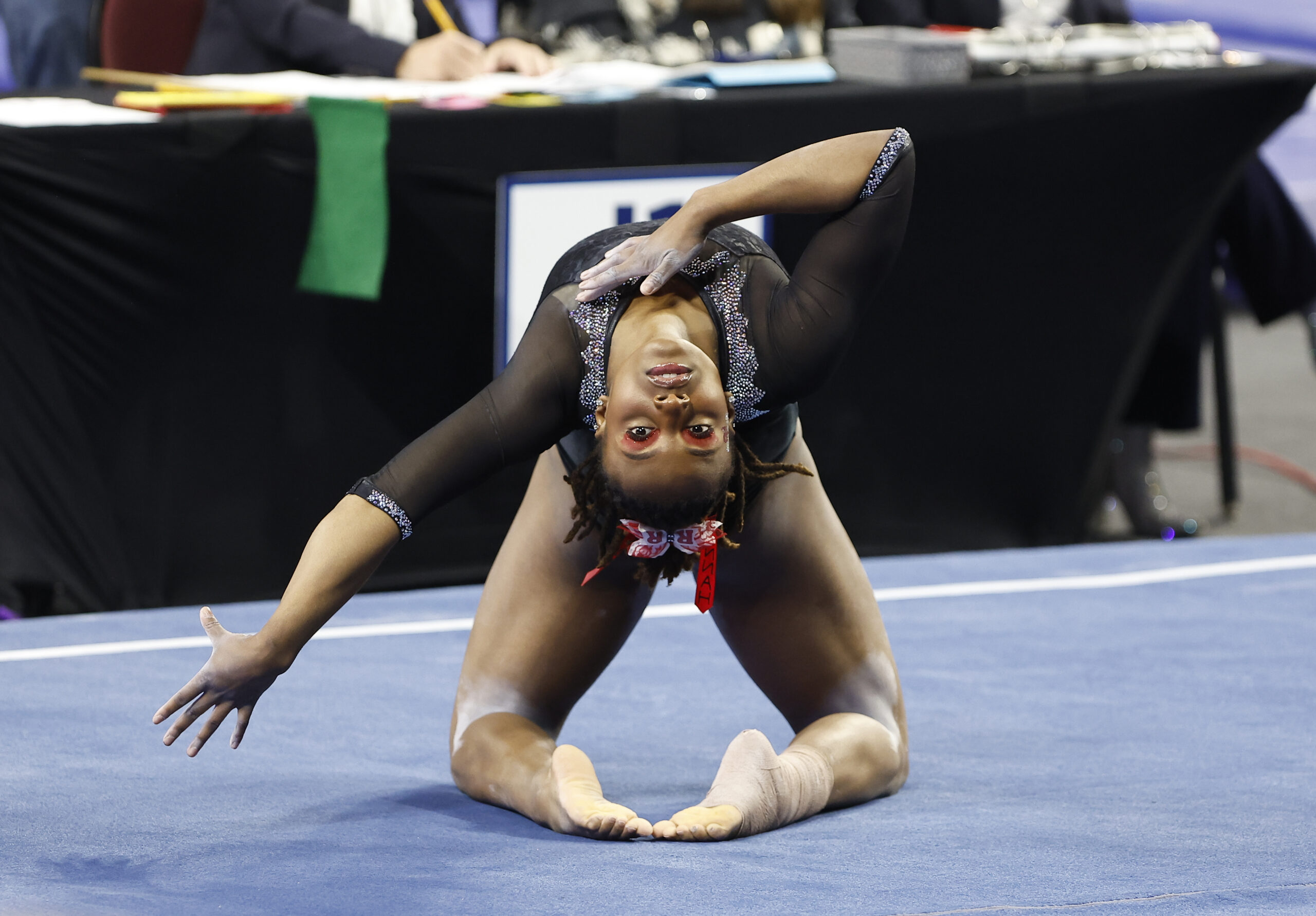 A gymnast in a black leotard performs a move on floor exercise.