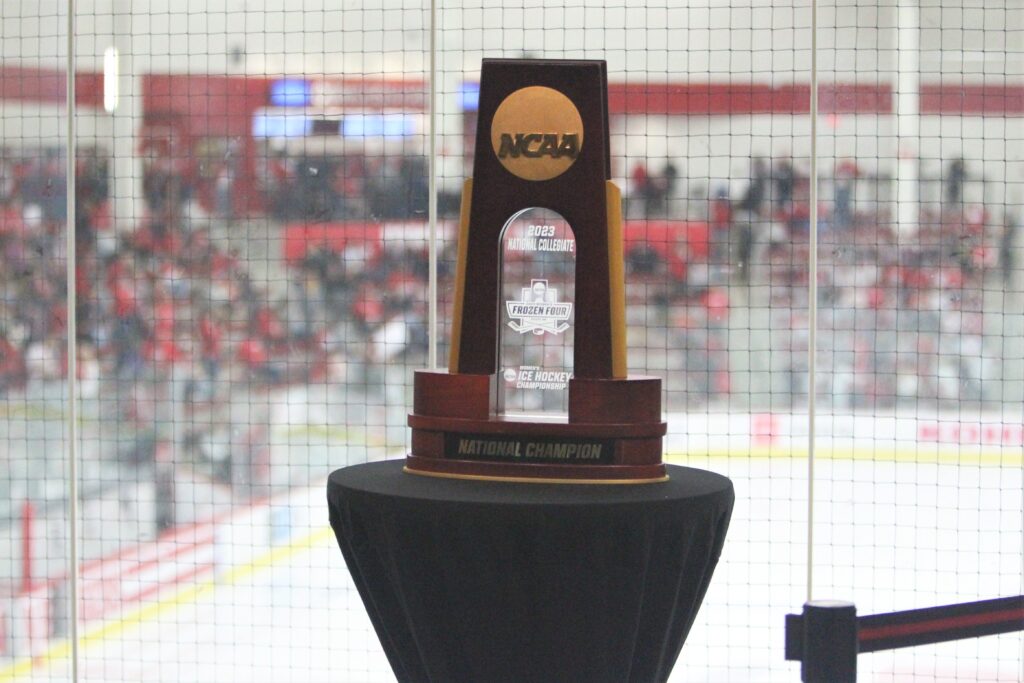 NCAA women's hockey championship trophy is on display with a hockey rink in the background
