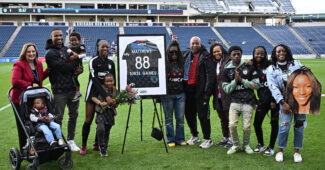 Chicago star player Cheyna Matthews is pictured with her family and Chicago Red Star front office staff, standing on a soccer field in front of a framed No. 88 jersey