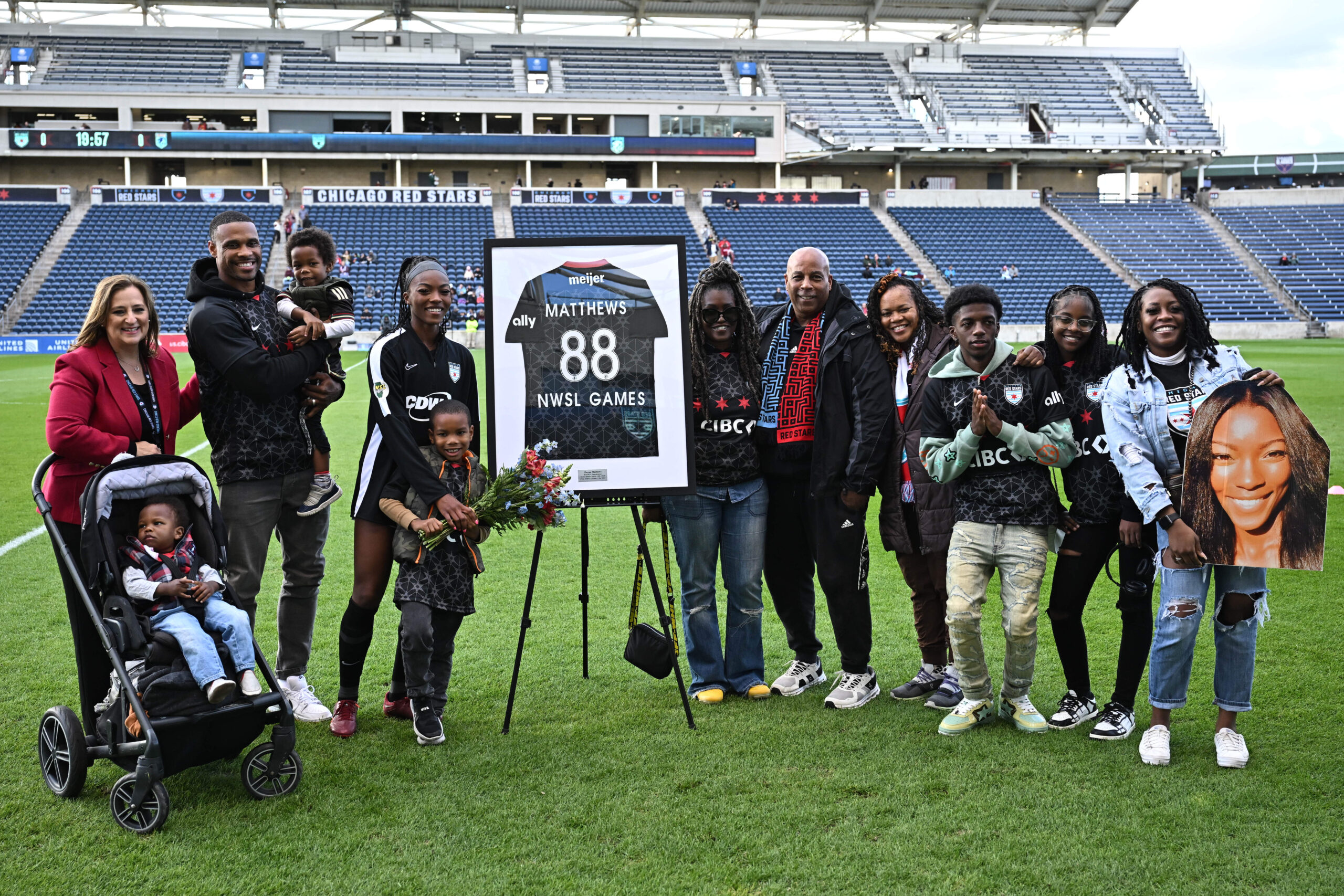 Chicago star player Cheyna Matthews is pictured with her family and Chicago Red Star front office staff, standing on a soccer field in front of a framed No. 88 jersey